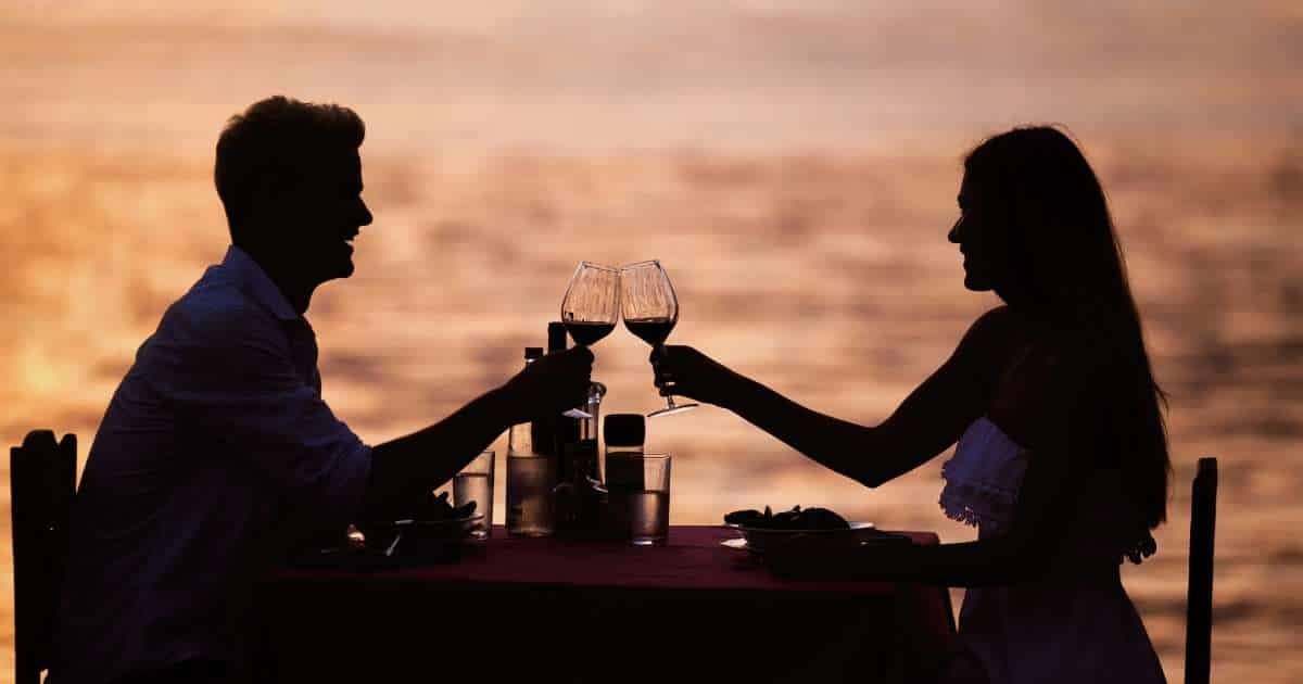 Man and woman toasting at a sunset dinner along the ocean.
