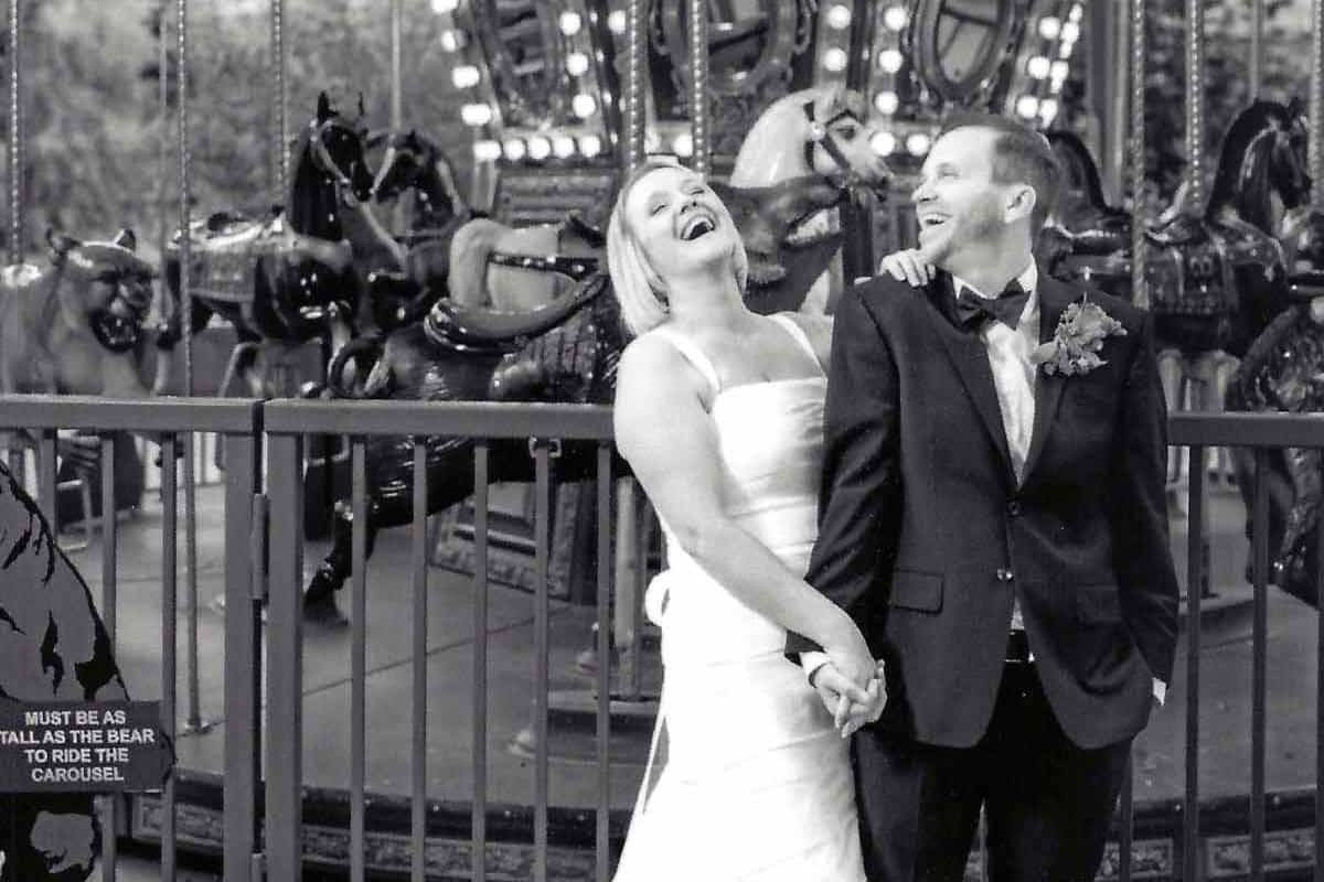 Happy couple laughing with each other in front of a carousel on their wedding day