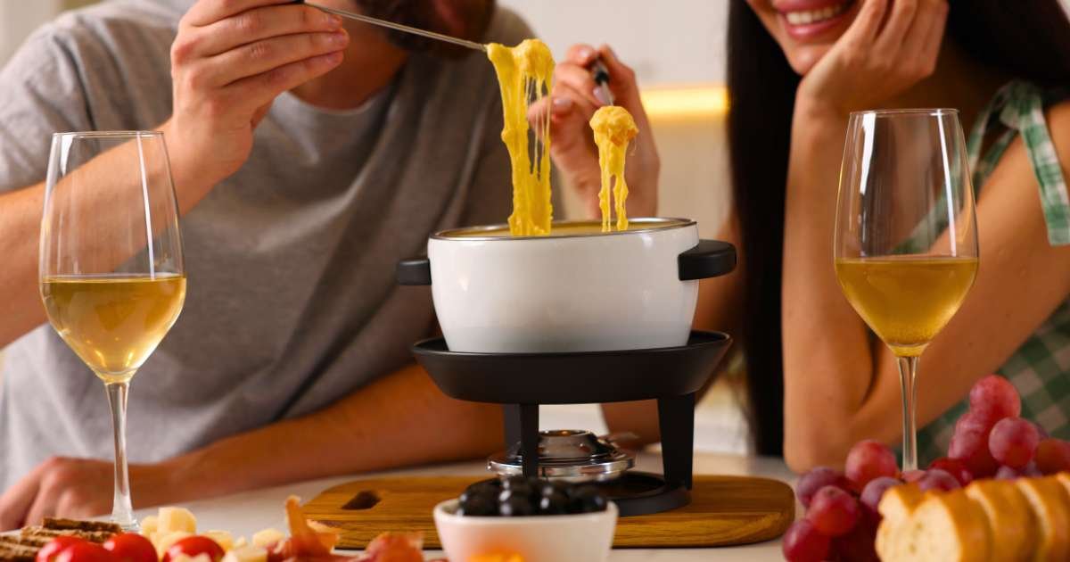 a table with a couple in their 40s sharing cheese fondue with two glasses of white wine