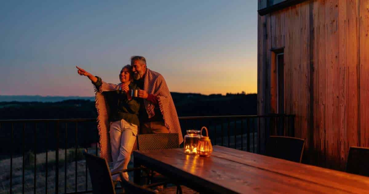 man and woman standing on an outdoor deck pointing up at the night sky while enjoying a cozy date