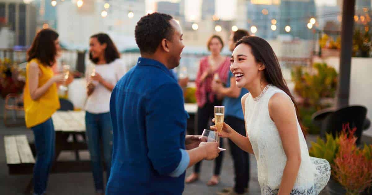 a man and woman mingling with a glass of champagne on a rooftop patio