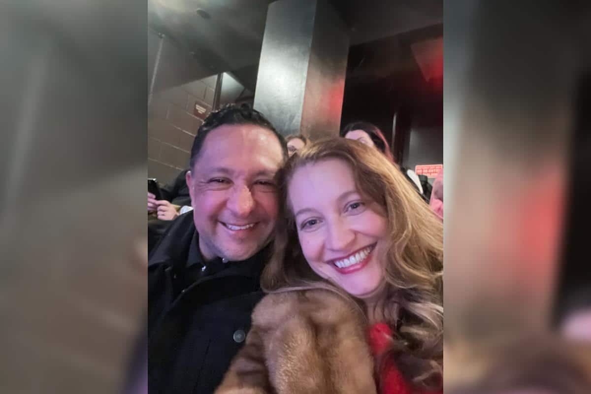 A casual selfie of Juan and Allyson sitting close together at a public event. They are smiling happily.