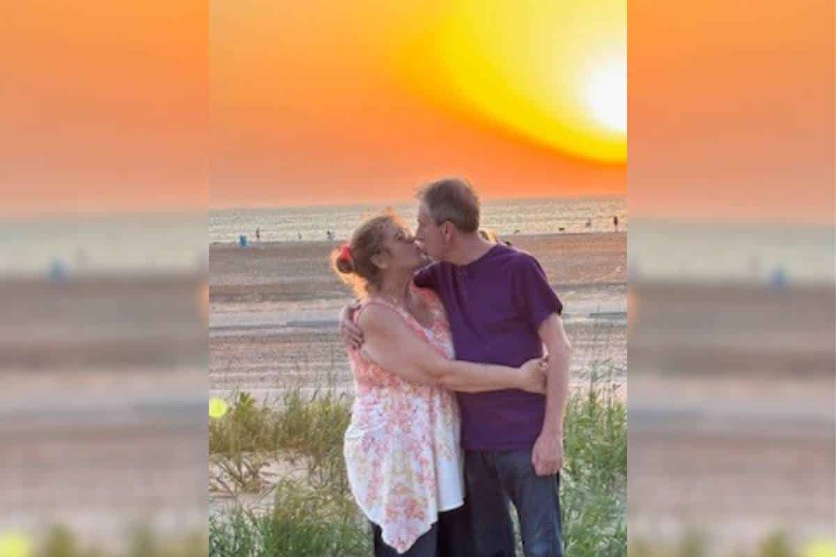 Don and Sandy embracing and sharing a kiss on the beach, in front of a beautiful sunset.