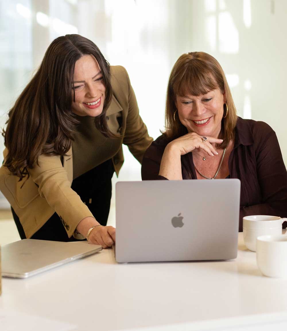 Two professional matchmakers collaborating over a laptop in a bright office